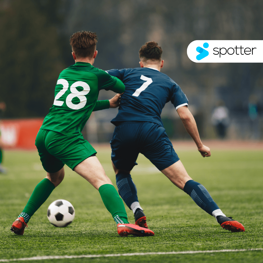 Two soccer players in green and blue jerseys competing for the ball, with the Spotter logo in the top right corner.